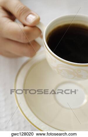 Stock Image - Close-up of a person's hand holding a cup of black tea. Fotosearch