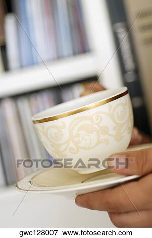 Stock Photo - Close-up of a person's hand holding a cup of tea and a saucer. Fotosearch