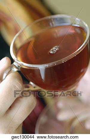 Picture - Close-up of a person's hand holding a cup of herbal tea. Fotosearch