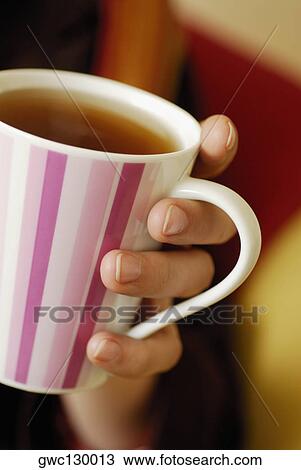 Stock Image - Close-up of a person's hand holding a cup of black tea. Fotosearch