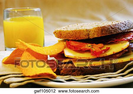 Stock Image - Close-up of orange juice with a sandwich and potato chips. Fotosearch