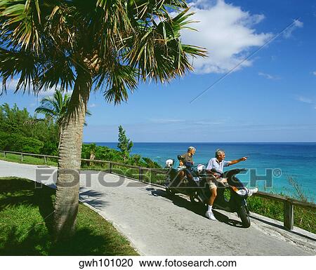 Stock Image - High angle view of a senior couple riding scooters, Bermuda. Fotosearch