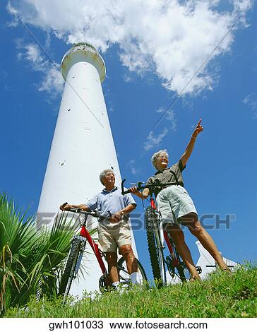 Stock Image - Low angle view of a senior couple standing in front of a tower with their bicycles, Bermuda. Fotosearch