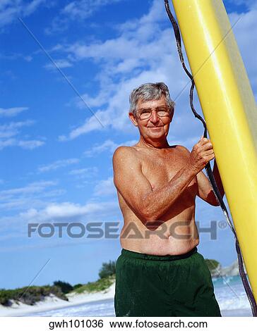 Stock Photograph - Low angle view of a senior man holding a surfboard, Bermuda. Fotosearch