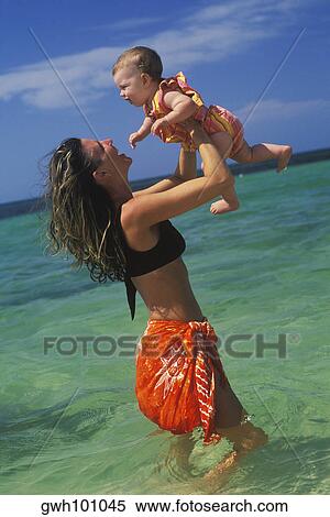 Side profile of a young woman carrying a baby girl in water View Large Photo Image Stock Photography - Side profile of a young woman carrying a baby girl in water. Fotosearch