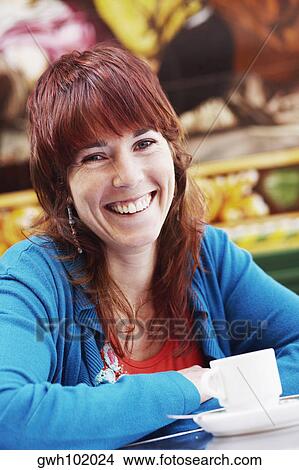 Portrait of a young woman sitting at a table with a cup of coffee in front of her View Large Photo Image Picture - Portrait of a young woman sitting at a table with a cup of coffee in front of her . Fotosearch