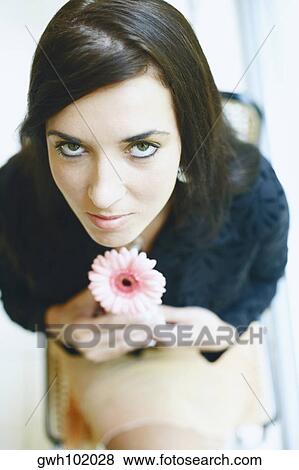 Portrait of a young woman sitting on a chair and holding a flower View Large Photo Image Stock Photo - Portrait of a young woman sitting on a chair and holding a flower. Fotosearch