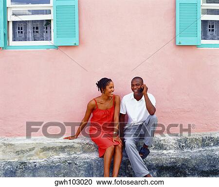 Young couple sitting in front of a house and talking on a mobile phone, Bermuda View Large Photo Image Stock Image - Young couple sitting in front of a house and talking on a mobile phone, Bermuda. Fotosearch