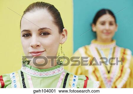 Stock Image - Portrait of a young woman smiling with another young woman standing in the background. Fotosearch