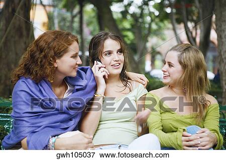 Close-up of a young woman talking on a mobile phone and sitting with her two friends View Large Photo Image Stock Photo - Close-up of a young woman talking on a mobile phone and sitting with her two friends. Fotosearch
