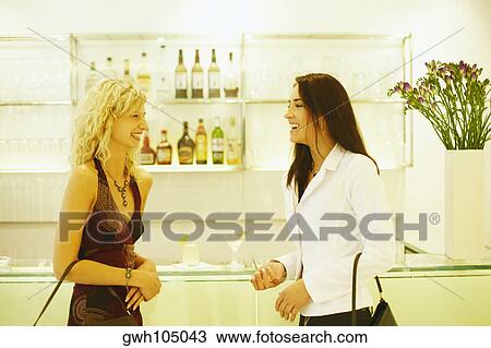 Stock Image - Side profile of two young women talking. Fotosearch