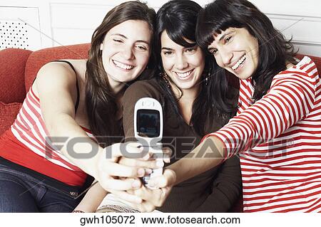 Two young women and a mid adult woman taking a photograph of themselves with a mobile phone View Large Photo Image Stock Image - Two young women and a mid adult woman taking a photograph of themselves with a mobile phone. Fotosearch