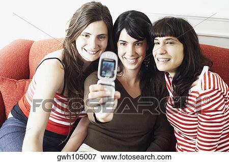 Stock Photo - Two young women and a mid adult woman taking a photograph of themselves with a mobile phone. Fotosearch