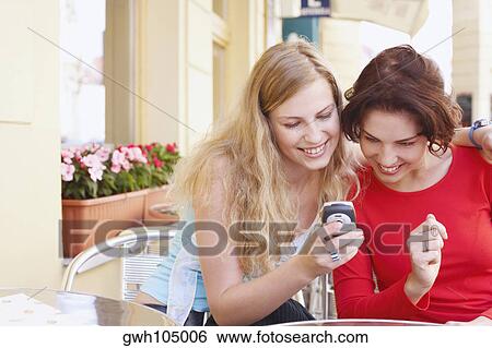 Two young women looking at a mobile phone and smiling View Large Photo Image Stock Photograph - Two young women looking at a mobile phone and smiling. Fotosearch