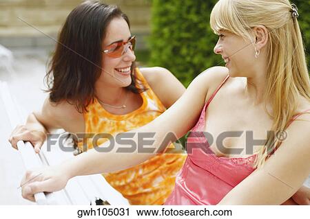 Two young women sitting on a bench View Large Photo Image Stock Image - Two young women sitting on a bench. Fotosearch