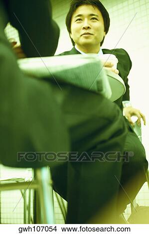 Low angle view of two businessmen sitting at a table View Large Photo Image Picture - Low angle view of two businessmen sitting at a table. Fotosearch