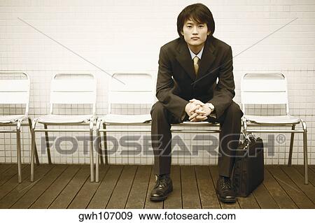 Stock Photo - Portrait of a businessman sitting on a chair with a briefcase. Fotosearch