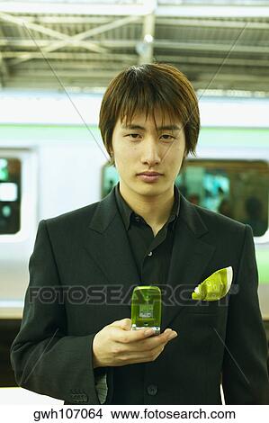 Portrait of a young man holding a mobile phone View Large Photo Image Picture - Portrait of a young man holding a mobile phone. Fotosearch