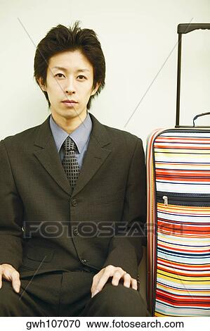 Stock Image - Portrait of a young man sitting with his hands on his knees. Fotosearch