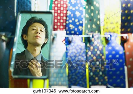 Reflection of a young man adjusting his tie in the mirror of a tie shop View Large Photo Image Stock Photograph - Reflection of a young man adjusting his tie in the mirror of a tie shop . Fotosearch