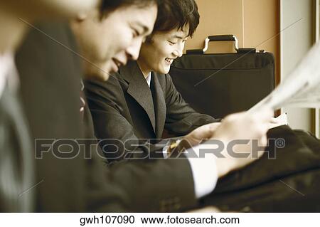 Side profile of a businessman reading a newspaper with another smiling in the background View Large Photo Image Stock Image - Side profile of a businessman reading a newspaper with another smiling in the background. Fotosearch