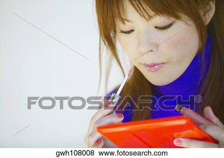 Stock Photo - Close-up of a young woman applying lipstick. Fotosearch
