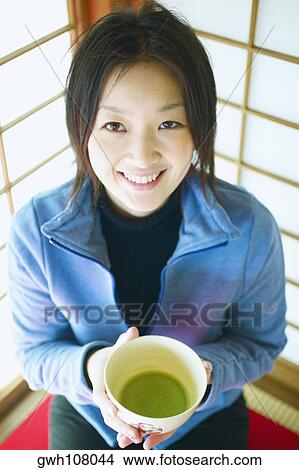 Picture - High angle view of a young woman holding a bowl of herbal tea and smiling. Fotosearch