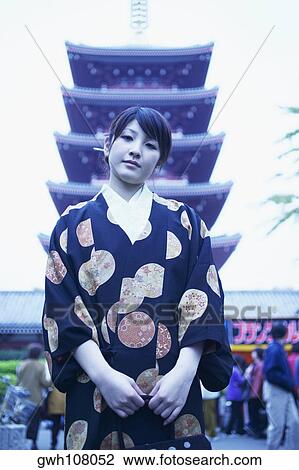 Stock Image - Low angle view of a young woman standing in front of a pagoda . Fotosearch