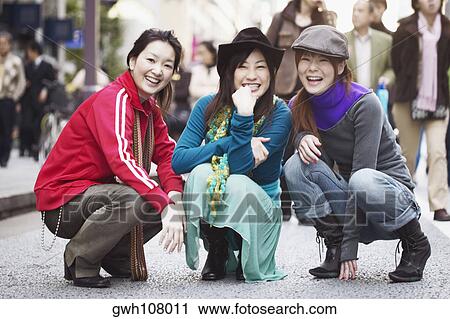 Stock Image - Portrait of three young women squatting on the street . Fotosearch