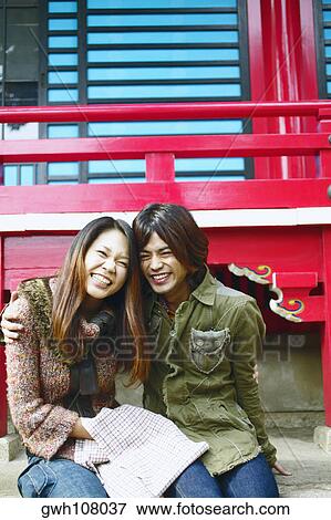 Stock Photo - Young woman and a mid adult man sitting together and smiling . Fotosearch
