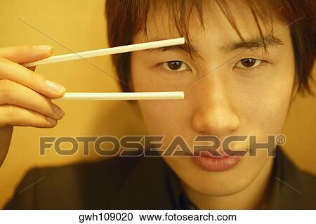 Stock Image - Close-up of a young man holding chopsticks. Fotosearch