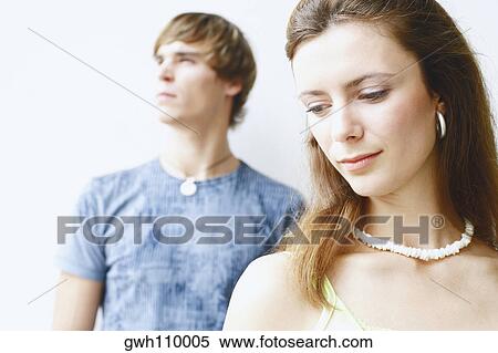 Close-of a young woman looking down with a young man behind her View Large Photo Image Stock Photography - Close-of a young woman looking down with a young man behind her. Fotosearch