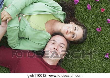 Stock Image - High angle view of a mid adult man and a young woman lying on the grass and smiling. Fotosearch