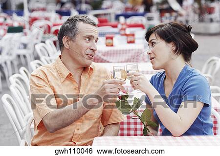Stock Photograph - Mature man and a young woman toasting at a sidewalk cafe . Fotosearch