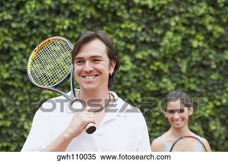 Mid adult man and a young woman holding tennis rackets and smiling View Large Photo Image Stock Photography - Mid adult man and a young woman holding tennis rackets and smiling. Fotosearch