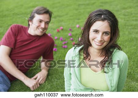 Stock Photo - Portrait of a young woman smiling with a mid adult man lying on the grass. Fotosearch