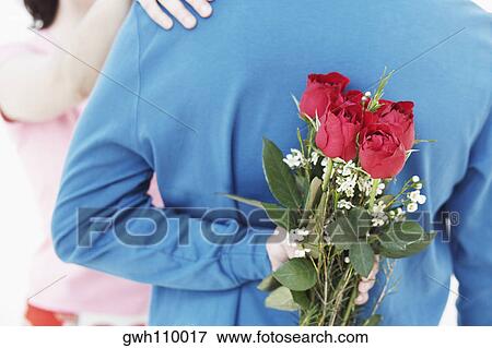 Rear view of a young man hiding a bunch of roses behind his back View Large Photo Image Stock Photo - Rear view of a young man hiding a bunch of roses behind his back. Fotosearch