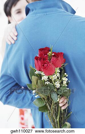 Rear view of a young man hiding a bunch of roses behind his back View Large Photo Image Stock Photo - Rear view of a young man hiding a bunch of roses behind his back. Fotosearch