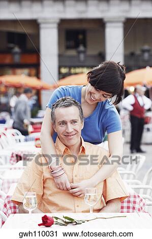 Stock Image - Young woman with her arm around a mature man at a sidewalk cafe . Fotosearch