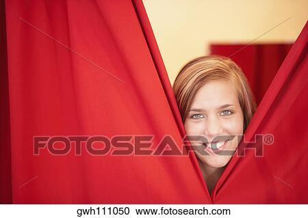 Stock Image - Portrait of a young woman standing behind a curtain. Fotosearch