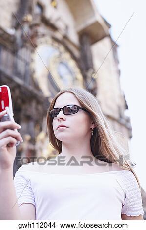 Low angle view of a young woman holding a mobile phone View Large Photo Image Picture - Low angle view of a young woman holding a mobile phone . Fotosearch