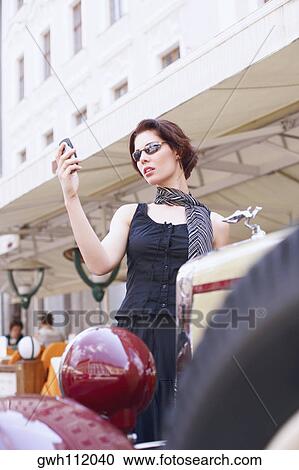 Low angle view of a young woman holding a mobile phone View Large Photo Image Stock Image - Low angle view of a young woman holding a mobile phone . Fotosearch
