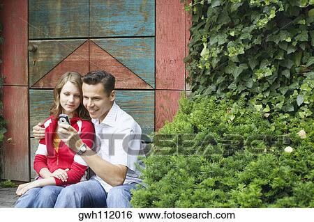 Stock Photograph - Mid adult man and a teenage girl looking at a mobile phone . Fotosearch