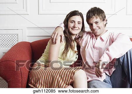 Portrait of a young couple sitting on a couch and smiling View Large Photo Image Stock Photography - Portrait of a young couple sitting on a couch and smiling. Fotosearch