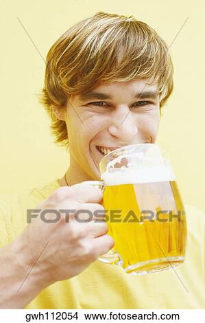 Portrait of a young man holding a glass of beer View Large Photo Image Picture - Portrait of a young man holding a glass of beer . Fotosearch
