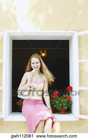 Portrait of a young woman holding an ice-cream cone and sitting in a window View Large Photo Image Stock Image - Portrait of a young woman holding an ice-cream cone and sitting in a window . Fotosearch