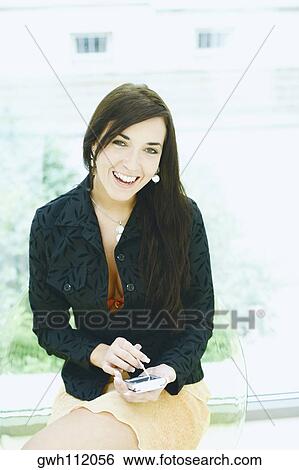 Stock Photograph - Portrait of a young woman operating a hand held device with a digitized pen. Fotosearch