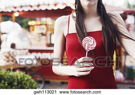 Stock Image - Mid section view of a woman holding a lollipop . Fotosearch