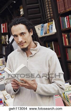 Portrait of a young man holding a book in a library View Large Photo Image Picture - Portrait of a young man holding a book in a library . Fotosearch