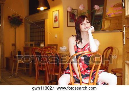 Stock Photo - Young woman sitting on a chair with her hand on her chin. Fotosearch